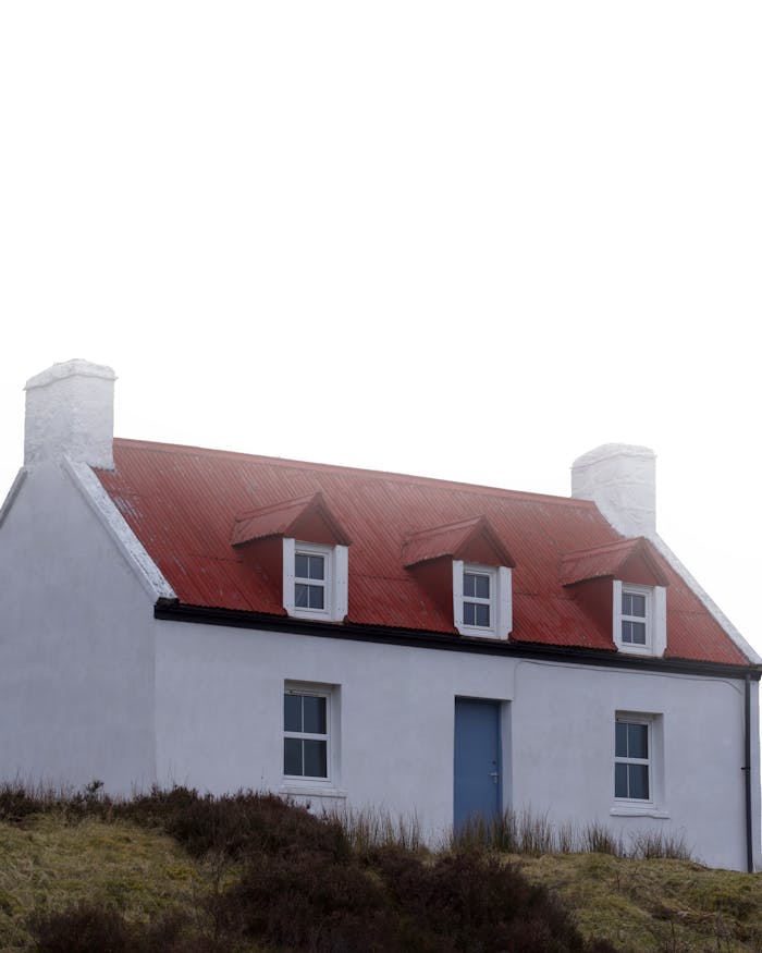 Charming white cottage with red roof in Scotland set against cloudy skies.